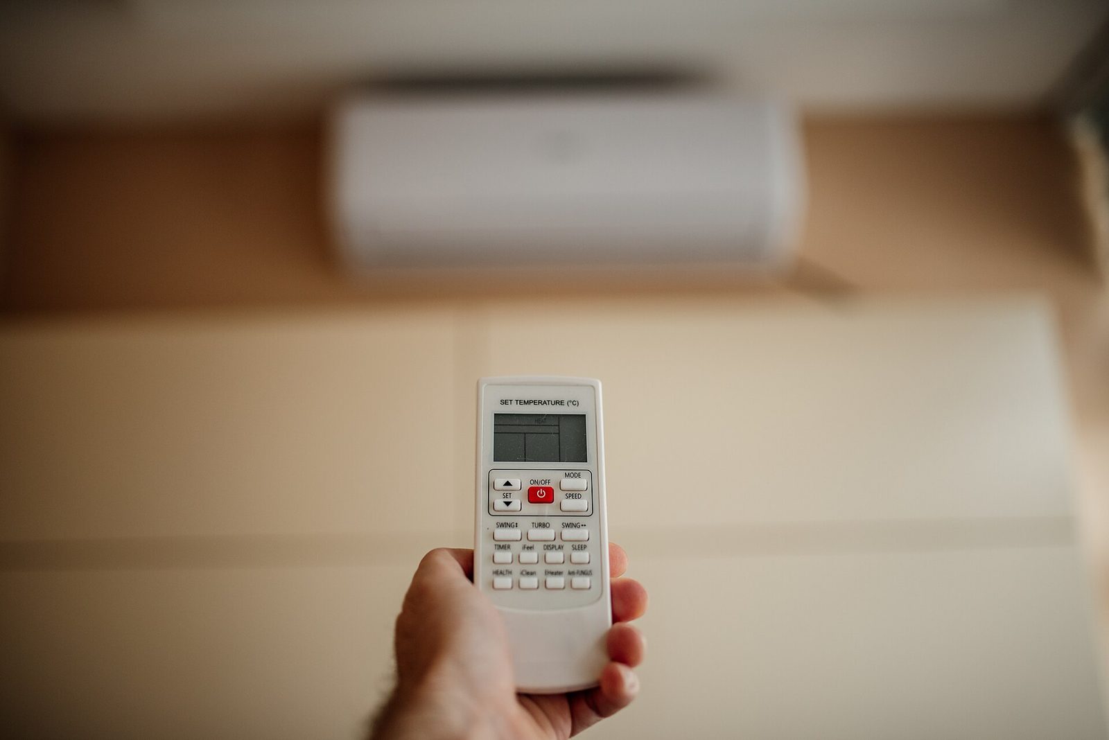Hand houdt een afstandsbediening met temperatuurdisplay vast, met een onscherpe wandairco op de achtergrond